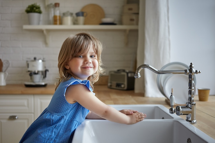 charming-little-girl-in-blue-dress-washing-hands-in-kitchen-cute-female-kid-looking-and-smiling-at-camera-helping-mother-doing-dishes-standing-at-sink-kids-childhood-cooking-and-housework_343059-682.jpg