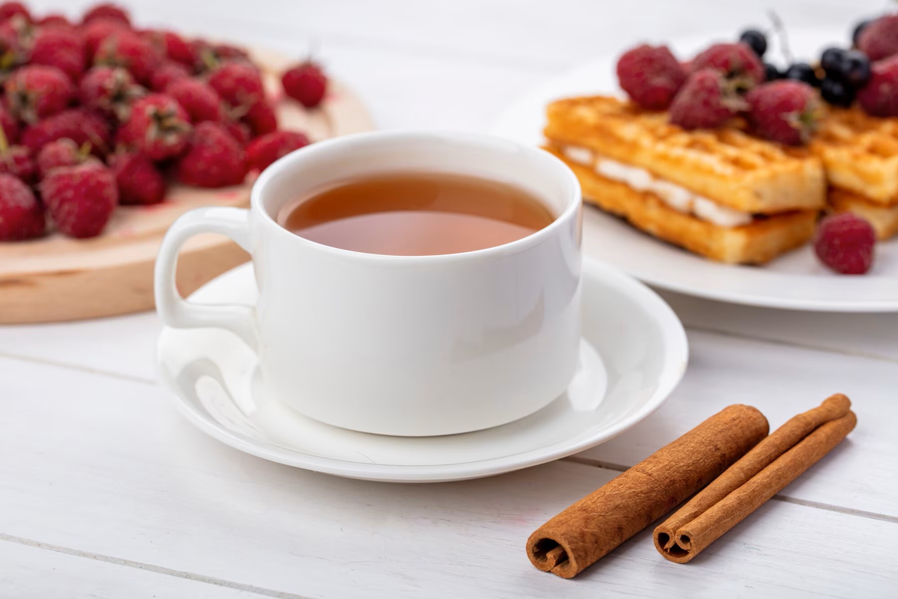 side-view-of-cup-of-tea-with-cinnamon-white-cherries-and-sweet-waffles-with-raspberries-on-a-white-surface_141793-17924.jpg