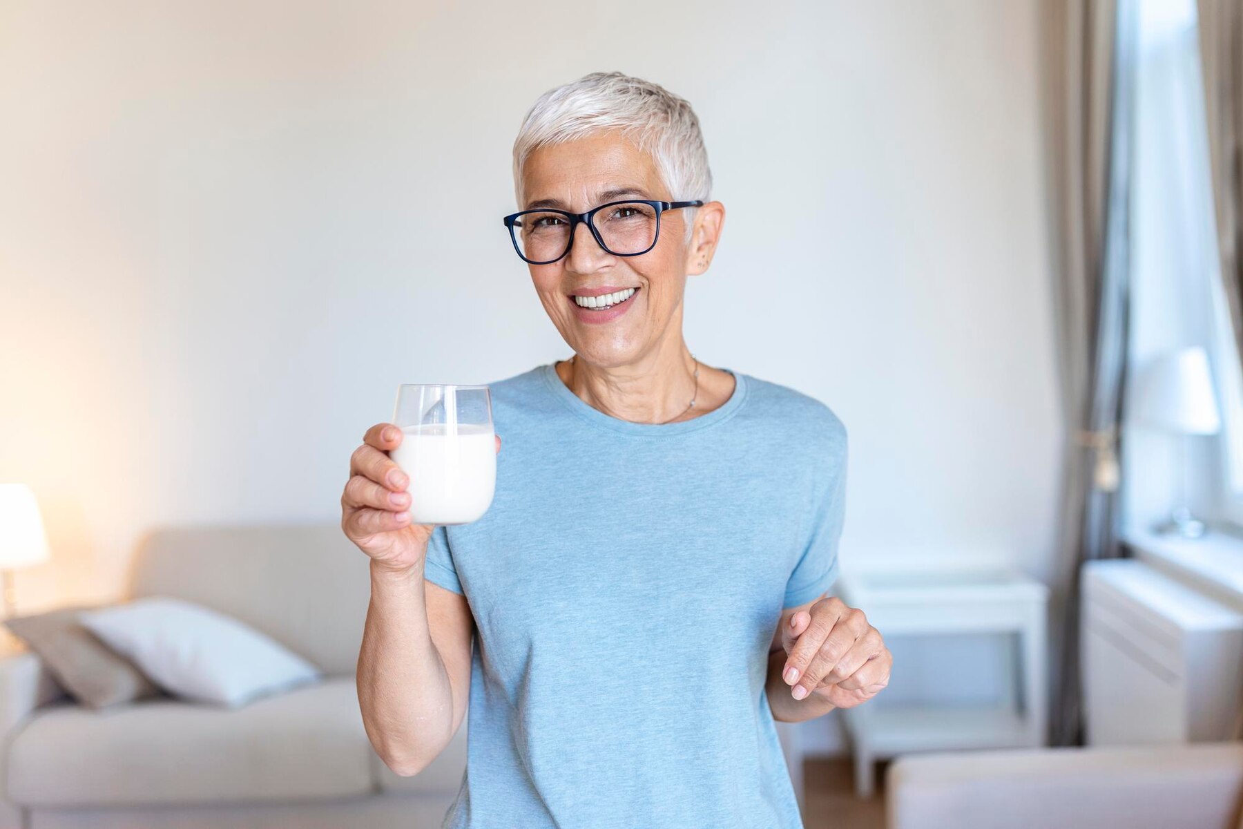 senior-woman-holding-glass-of-milk-at-home-middle-age-woman-drinking-a-glass-of-fresh-milk-with-a-happy-face-standing-and-smiling-with-a-confident-smile-showing-teeth_657921-222.jpg