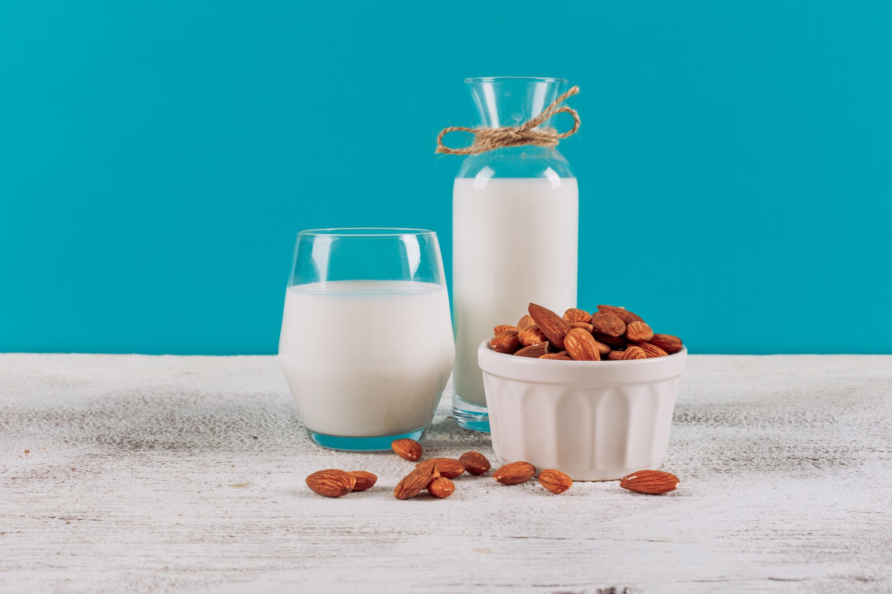 bottle-of-milk-with-glass-of-milk-and-bowl-of-almonds-side-view-on-a-white-wooden-and-blue-background_176474-4591.jpg